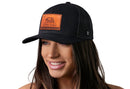 A woman with long brown hair smiles while wearing the Haka Hat California Flag Trucker Hat Leather | Black CA Snapback by Haka Hat, which features an orange patch with a bear and "California Republic" on a plain white background.