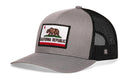 The Haka Hat California Flag Trucker Hat features a gray-black design, a front patch with the California Republic bear, red star, and stripes. It includes a mesh back and adjustable snapback strap. Brand: Haka Hat.