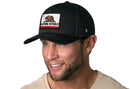 A smiling man wears a black Haka Hat California Flag Trucker Hat snapback with a California Republic bear patch and a beige shirt, shown against a white background.