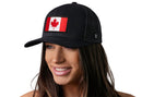 A woman with long brown hair smiles while wearing the Haka Hat Canada Flag Trucker Hat, a black Canadian snapback by Haka Hat featuring an embroidered Canada flag patch. The background is white.