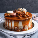 A cake featuring macarons, chocolate pieces, caramel popcorn, and SALTOPIA Infused Sea Salts’ ROOM FOR DESSERT Vanilla Bean & Salted Caramel Sugar sits on a white stand against a dark background.