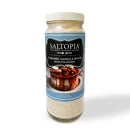A clear jar labeled SALTOPIA Vanilla Bean & Salted Caramel Sugar: ROOM FOR DESSERT has a blue label with a dessert image. Filled with fine, light brown vanilla bean sugar, it’s perfect for fans of flavored sugars. Brand: SALTOPIA Infused Sea Salts.