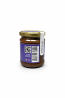 A glass jar from Taycte, featuring a gold lid and a purple label with the Taycte logo, displays both a QR code and barcode. A white sticker reading “WARRANTY VOID IF SEAL IS BROKEN” is also attached. Inside the jar is Taycte Taycte Organic Hazelnut Cocoa Cream—a brown, organic spread.
