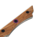 Close-up of the Messermeister Chef Claudette Zepeda 7" Knife handle with three screws, including one with a purple ring. This limited-edition chef's knife has smooth curves, polished finish, and striking wood grain against a white background.