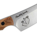 A close-up of the Messermeister Chef Claudette Zepeda Chef's Knife - 7" shows its wooden handle and a blade engraved with her name plus two flowering prickly pear cacti, capturing the knife’s Mexican-inspired design.
