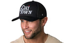 A man smiles and looks to the side, wearing a Haka Hat Chi Town White Script Trucker Hat—an Illinois snapback in black with "CHI TOWN" embroidered in white and a red star.