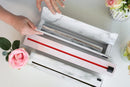 A person opens two ChicWrap Carrara Marble Aluminum Foil Refillable Dispensers (12" x 30'). Pink roses in vases and a green leaf sit on the table beside the stylish cases.