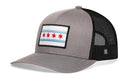 The Haka Hat Chicago Flag Trucker Hat features a gray-black design, mesh back, snapback closure, and a front patch with two blue stripes and four red stars inspired by the city flag.