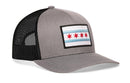 The Haka Hat Chicago Flag Trucker Hat features a gray-black design with mesh back, a front patch showing blue stripes and four red stars, plus an adjustable snapback closure.