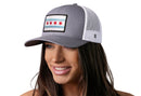 A woman smiles, wearing the Haka Hat Chicago Flag Trucker Hat—a gray-white city snapback with a Chicago flag patch on the front and white mesh back.