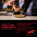 A bartender rims a cocktail glass with The Spice Lab Chili Lime Margarita Salt Cocktail Rimmer, beside a plate of the vibrant margarita salt and two red chili peppers on the bar counter. Text provides instructions for using The Spice Lab’s cocktail rimmer.
