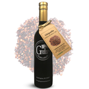 A dark glass bottle of Georgetown Olive Oil Co CHIPOTLE Infused | High Polyphenols Extra Virgin Olive Oil, adorned with a tan tag and gold tie featuring the Georgetown Olive Oil Co. logo, is displayed in front of a mound of crushed chipotle peppers.