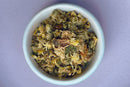A white bowl filled with World Spice Chrysanthemum Flower, by World Spice, sits on a light purple surface—perfect for brewing a caffeine-free tea with a delicate floral aroma.