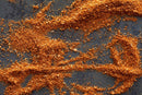 Orange-brown spices from the World Spice Americana Tasting Flight by World Spice are scattered in uneven lines and swirls on a dark surface, resembling abstract art or brush strokes—a visual representation of the aromatic blends featured in this USA regional spice collection.