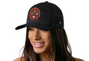 A woman with long brown hair smiles while wearing a Haka Hat Cleveland Trucker Hat | Black CLE X Football Snapback, which features an orange and white circular logo on the front. The background is white.