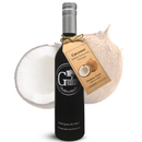 A bottle of Georgetown Olive Oil Co. Coconut White Balsamic, complete with a tag featuring a coconut image and product details, stands in front of a halved coconut. The tag also notes that this unique balsamic is crafted in Modena, Italy by Georgetown Olive Oil Co.
