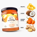 A jar of Texan Heartland Coconut Pineapple Habanero Hot Jam next to labels pointing to its ingredients: pineapple chunks, a coconut, habanero peppers, and ginger root.