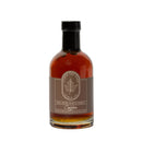 A glass bottle of Under The Bark Syrup Co Coffee Maple Syrup features a brown label with a leaf logo, a black cap, and amber coffee-flavored syrup visible inside. Brand: Under The Bark Syrup Co.