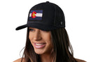 A woman with long brown hair smiles while wearing a Haka Hat Colorado Flag Trucker Hat | Black CO Snapback by Haka Hat, featuring a Colorado flag patch on the front, against a white background.