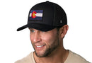 A man smiles wearing a Haka Hat Colorado Flag Trucker Hat—Black CO Snapback, highlighting the iconic Colorado flag patch.