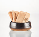 Three “Wooden Beard Combs” by The Immaculate Beard, each featuring fine and wide teeth, are displayed upright in a small, round ceramic bowl with a dark upper half and natural brown base, set against a white background—making them an essential addition to any beard grooming routine.