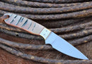 The Texan Knives Handmade Buckaroo Belt Knife features a polished J2 steel blade, unique sheep horn handle with natural patterns, and comes with a Western leather sheath—perfectly displayed on coiled, weathered ropes.