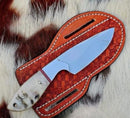 The Texan Knives Custom Handmade Bull Cutter Knife with a J2 steel blade and bone handle comes with a brown leather sheath, displayed on white and brown cowhide.