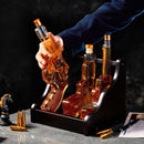 A hand lifts a revolver-shaped bottle from the Craftgen 3 Gun Whiskey Decanter Set by Craftgen, featuring three lead-free borosilicate glass bottles in a dark wooden holder with bullet accents and a chess knight—ideal for any whiskey bar display.