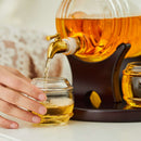A hand pours golden whiskey from the Craftgen Barrel Whiskey Decanter Set with a brass spout, displayed on a black stand—an elegant centerpiece for any home bar by Craftgen.