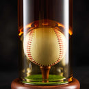 The Craftgen Baseball Decanter Set by Craftgen features a glass display dome on a wooden base with green felt, illuminated by warm light against a dark background—an ideal baseball gift for collectors and fans.
