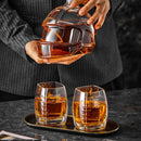 A person in a pinstripe suit holds the Craftgen Football Whiskey Decanter by Craftgen, filled with amber liquor, while two matching football-stitched glasses rest on a tray—an eye-catching gift and must-have game day barware.