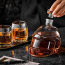 A hand removes the stopper from the Craftgen Football Whiskey Decanter by Craftgen, shaped like a football helmet and filled with amber liquor. Two matching glasses sit on a tray nearby—a standout piece of game day barware.