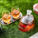 The Craftgen Football Whiskey Decanter by Craftgen, filled with whiskey, sits on turf beside a football and two glasses—an eye-catching barware piece and a unique addition to any whiskey gift collection.
