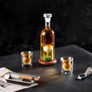 The Craftgen Golf Liquor Decanter Set by Craftgen features a golf whiskey decanter with a gold golf ball inside on a wooden base, two matching glasses, and makes the ideal refined gift for golf enthusiasts.