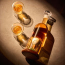 The Craftgen Golf Liquor Decanter Set by Craftgen features a whiskey decanter with a golf ball in its base beside two filled glasses—perfect for unique golf gifts.