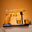 The Craftgen Gun Whiskey Decanter Set by Craftgen features a glass gun-shaped decanter with amber liquid, two shot glasses, and bullet accents on a wooden stand—an eye-catching home bar gift displayed against a warm orange background.