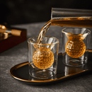 A drink is being poured into a Craftgen Golf Decanter Set double-walled glass with a golf ball-shaped chamber, while another identical glass and wooden box rest on a black and gold tray—an ideal whiskey gift from Craftgen.