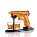 The Craftgen Gun Whiskey Decanter Set by Craftgen features a glass gun decanter filled with whiskey, resting horizontally on a stand with two shot glasses beneath the barrel, all displayed on a black base—a striking gift for any home bar.