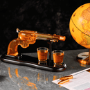 The Craftgen Gun Whiskey Decanter Set by Craftgen includes a glass gun-shaped decanter with amber liquid, two matching shot glasses, and a black stand—perfect for adding a western touch to your barware collection.