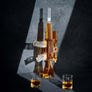 The Craftgen Rifle Whiskey Decanter Set by Craftgen features a striking decanter filled with whiskey, standing upright between two matching glasses on a dark surface with dramatic lighting casting bold shadows.