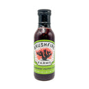 A bottle of Brushfire Farms Cranberry Pepper Sauce, distinguished by its green label adorned with a vibrant cactus and flames graphic. Inside is a dark red holiday sauce that brings a bold twist to both sweet and savory dishes—making it the perfect versatile condiment for any occasion.