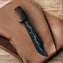 The Texan Knives Authentic Crocodile Dundee Knife 16" with a J2 steel blade and brass guard rests on tan leather atop wood, featuring a distinctive jagged white line.