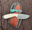 Two Texan Knives Cowboy Bull Cutter knives with custom handmade Damascus steel blades and resin handles—one white, one turquoise—rest on a brown leather sheath atop quilted brown fabric.