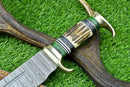 A close-up of the Texan Knives Custom Handmade Damascus Steel Bowie Knife with a 16" blade, featuring an ornate stag horn handle, displayed on antler atop green grass; includes a leather sheath.