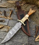 The Texan Knives Custom Handmade Damascus Steel Bowie Knife features a 13-inch patterned blade, bone handle with brass guard, and comes with a leather sheath. It is displayed on stone alongside antler pieces and twine.