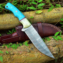 The Texan Knives Custom Handmade Damascus Steel Hunting Knife features a 10-inch blade and resin handle, resting on its leather sheath atop logs surrounded by green leaves.