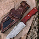 The Texan Knives Custom Handmade Damascus Steel Skinner Knife with a 4.5" blade and Padauk wood handle, by Texan Knives, rests beside a brown leather sheath with decorative stitching on a tree stump.