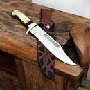 The Texan Knives Custom Handmade David Bowie Knife features a polished J2 steel blade and a camel bone handle, resting on wood with a patterned brown leather sheath beside it.