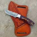 The Texan Knives Custom Handmade Fixed Blade Cowboy Knife – Damascus Steel Pine Cone Handle by Texan Knives rests on a brown floral-embossed leather sheath, displayed atop a stone surface.