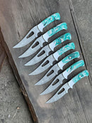Seven Texan Knives Custom Handmade Damascus Hunting Knives, each with patterned steel blades and marbled resin handles, are neatly lined up on a rustic wooden surface, all facing the same direction.